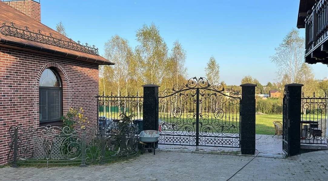 Тёмный забор с воротами у кирпичного дома